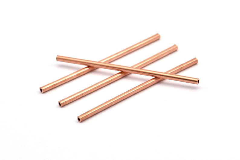 May include: Four copper coloured metal tubes, each with a hollow centre, are stacked on top of each other.