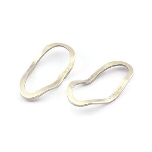 以下が含まれることがあります： 有機的で自由な形をしたシルバーのイヤリングのペア。イヤリングは滑らかで質感のある金属でできています。