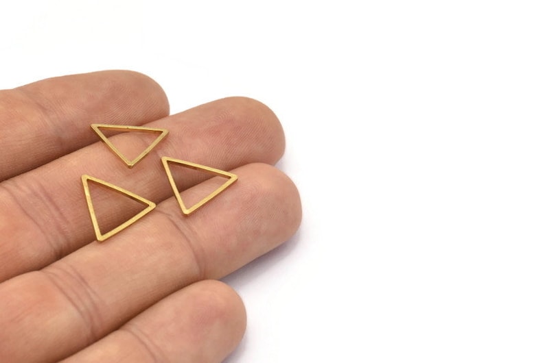 Puede incluir: Tres abalorios de metal de forma triangular de color dorado. Los abalorios est&aacute;n abiertos por un lado y tienen un acabado liso y pulido.