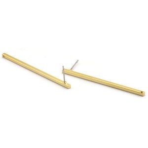 Può includere: Un paio di orecchini a barra color oro. Ogni orecchino è una barra sottile e rettangolare con un perno per forare. Gli orecchini sono esposti su uno sfondo bianco, mostrando il loro design semplice e moderno.