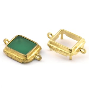 Puede incluir: Dos engastes de metal dorado para una piedra preciosa de forma cuadrada. Un engaste tiene una piedra preciosa verde en su lugar, mientras que el otro está vacío. Ambos engastes tienen un bucle en el lateral para sujetar a una cadena o cordón.