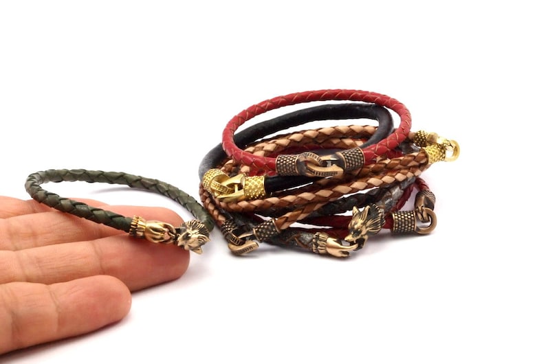K&ouml;nnte beinhalten: Ein Set aus f&uuml;nf Lederarmb&auml;ndern mit goldenen und messingfarbenen Akzenten. Die Armb&auml;nder sind geflochten und haben ein Wolfskopfdesign am Verschluss.
