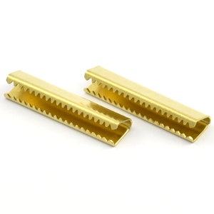 May include: Two gold metal slider buckles with a serrated edge. The buckles are designed to be used for attaching straps or cords.
