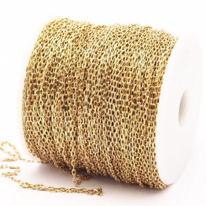 May include: A spool of gold-colored chain. The chain is made of small, interlocking oval links. The spool is white and has a central hole. The chain is partially unraveled, with a length of chain extending from the spool.