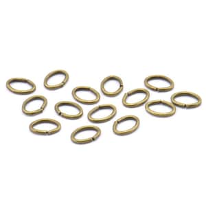 Puede incluir: Un grupo de 14 anillos de salto ovalados en acabado latón. Los anillos están dispersos sobre un fondo blanco.