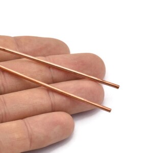 Puede incluir: Dos varillas delgadas de cobre, de aproximadamente 15 cm de largo, se sostienen en una mano. Las varillas son lisas y tienen un acabado met&aacute;lico brillante.