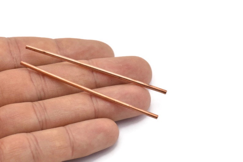 Puede incluir: Dos varillas delgadas de cobre, de aproximadamente 15 cm de largo, se sostienen en una mano. Las varillas son lisas y tienen un acabado met&aacute;lico brillante.