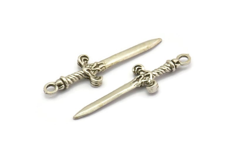 May include: Two silver sword charms with intricate details. The swords have a twisted handle and a pointed tip.