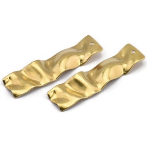 May include: A pair of gold-toned earrings with a wavy, textured design. The earrings are long and narrow, and they have a slightly curved shape.