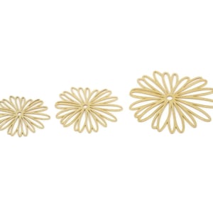 Pode incluir: Três ornamentos dourados em forma de flor vazada de tamanhos variados são dispostos sobre um fundo branco. A maior flor está à direita, a menor à esquerda e a de tamanho médio no centro.