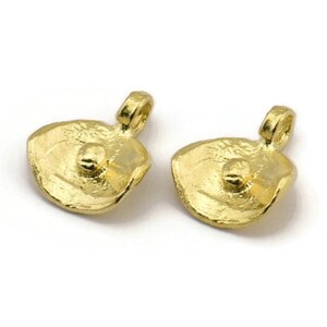 May include: Two gold-toned metal pendant charms with a textured, organic shape and a small round bead in the centre. Each charm has a loop at the top for attaching to a necklace or bracelet.