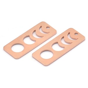 May include: Two rose gold metal charms with a crescent moon design. Each charm is rectangular with a hole at the top for attaching to a necklace or bracelet.