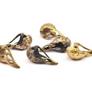 May include: Six small, detailed, brass bird skull charms. The charms are in various shades of gold and black, with some having a more aged look.