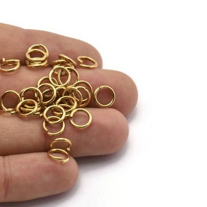 May include: A pile of gold jump rings, a type of jewelry finding, in a hand. The rings are small and round, and they are perfect for attaching charms, pendants, or other jewelry components.