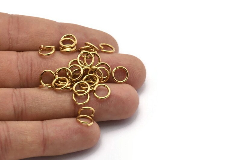 May include: A pile of gold jump rings, a type of jewelry finding, in a hand. The rings are small and round, and they are perfect for attaching charms, pendants, or other jewelry components.