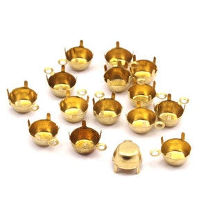 May include: A group of 14 gold-toned metal cup-shaped settings with prongs and a loop on the side. The settings are arranged in a semi-circle on a white background.