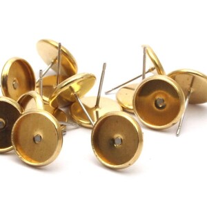 May include: A group of gold-toned earring settings with a round, flat base and a post for attaching earrings. The settings are designed to hold a variety of cabochons or other decorative elements.