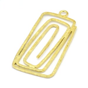 May include: Gold-toned metal pendant with a rectangular shape and a layered, abstract design. The pendant has a loop at the top for attaching to a chain or cord.