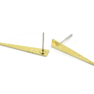May include: A pair of gold-toned earrings with a pointed, triangular shape. The earrings are made of metal and have a textured surface.