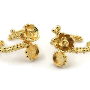 May include: Two gold-tone rings with a flower design and a round bezel setting. The rings are made of metal and have a delicate, feminine look.