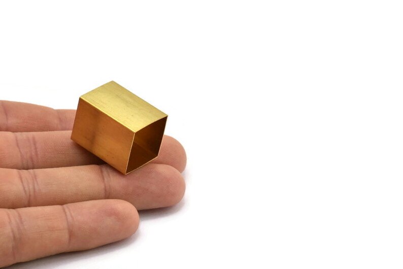 Puede incluir: Un peque&ntilde;o objeto cuadrado hueco hecho de lat&oacute;n. El objeto est&aacute; sentado en la mano de una persona.