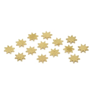May include: A collection of small, gold-colored star-shaped embellishments. Each star has eight points and a textured surface. The stars are scattered against a white background, suitable for crafting or decorative projects.