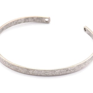 Könnte beinhalten: Ein silbernes Armreif-Armband mit gehämmerter Oberfläche.
