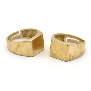 May include: Two gold-toned rings with square-shaped tops. The rings are simple and minimalist in design.