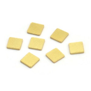 Könnte beinhalten: Sieben kleine, quadratische, goldfarbene Metallstücke auf weißem Hintergrund.