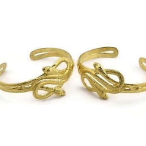 Peut inclure: Deux bracelets en forme de serpent dorés. Les bracelets sont en métal et présentent un motif de serpent détaillé.