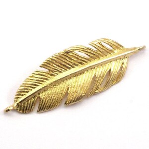 May include: A gold-colored metal feather charm with a detailed design. The feather is about 2 inches long and has a hole at the top for attaching to jewelry or other crafts.