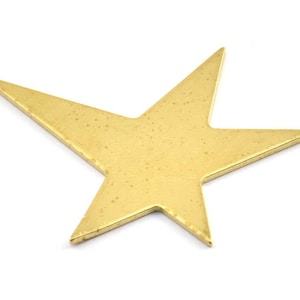 Puede incluir: Una estrella de metal de color dorado con cinco puntas. La estrella es plana y tiene una superficie ligeramente texturizada.