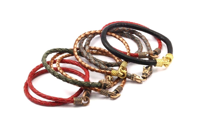 K&ouml;nnte beinhalten: Ein Set aus sechs Lederarmb&auml;ndern mit verschiedenen geflochtenen Lederfarben und Metall-Wolfs-Kopf-Verschl&uuml;ssen.