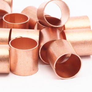 May include: A pile of copper pipe connectors, also known as copper couplings, in various sizes. The connectors are shiny and have a smooth, metallic finish.