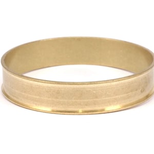 May include: A gold-colored metal ring with a wide band and a smooth, slightly textured surface.