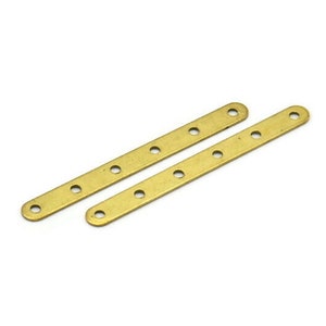 May include: Two gold metal strips with six evenly spaced holes each. The strips are straight and have rounded ends.