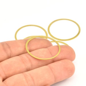 May include: Four gold-colored metal rings of varying sizes, stacked on top of each other. The rings are smooth and have a shiny finish.