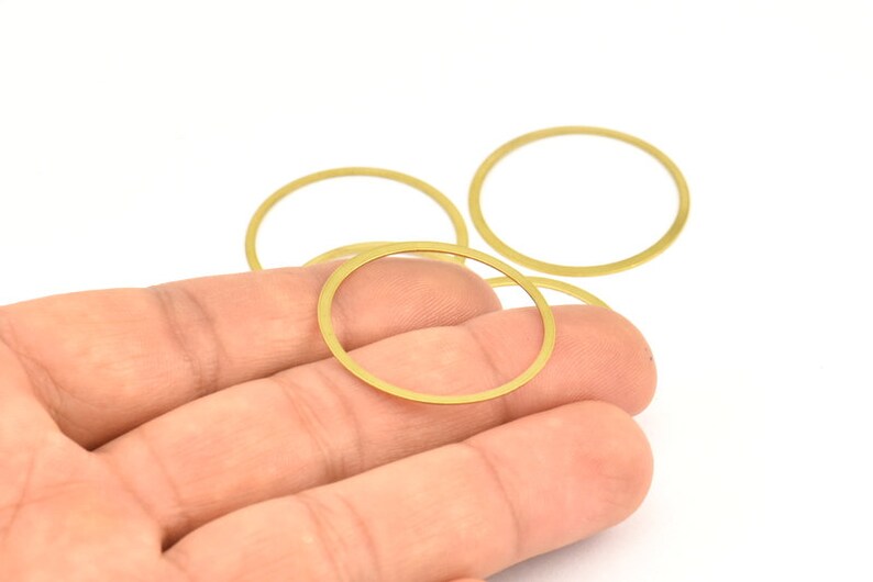 May include: Four gold-colored metal rings of varying sizes, stacked on top of each other. The rings are smooth and have a shiny finish.