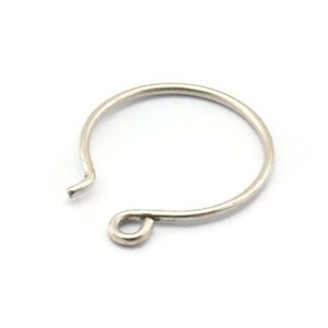 May include: A silver-colored earring hoop with an open design. The hoop is circular with a small loop at the bottom and a hook at the top. The earring is set against a white background.