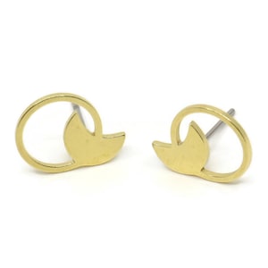 May include: A pair of gold-colored stud earrings. Each earring features a stylized design with a curved, open circle and a leaf-shaped element. The earrings are set against a white background.