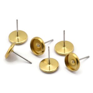 May include: Six gold-toned earring settings with silver posts. The settings are round and have a small indentation in the center.