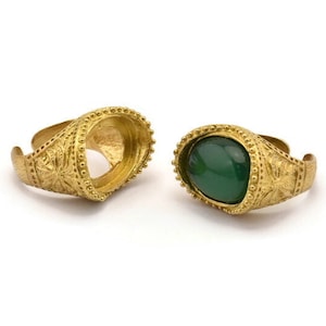 May include: Two gold rings with ornate designs. One ring has a green gemstone set in the center. The other ring is empty.