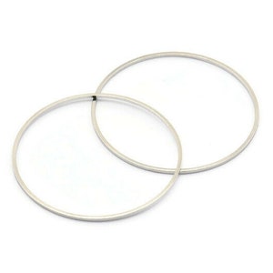 May include: Two silver-colored hoop earrings, each a perfect circle, are displayed against a white background. The earrings are thin and minimalist in design, with a smooth, reflective surface. The hoops are slightly overlapping.