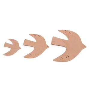 May include: Three wooden bird cutouts of different sizes, arranged from smallest to largest. Each bird is a light brown colour with small, dark brown dot details on the wings. The birds are set against a plain white background.