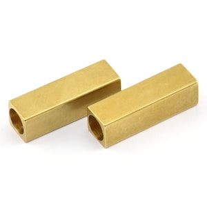Może przedstawiać: Dwa złote metalowe łączniki prętowe z pustym środkiem. Łączniki mają kształt prostokątny i gładkie, polerowane wykończenie.