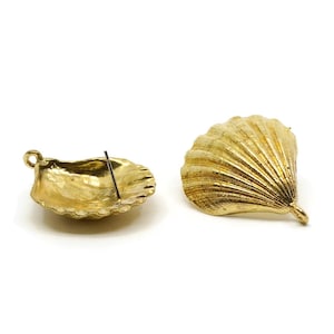 May include: Two gold-colored seashell-shaped earrings on a white background. One earring is a stud with a post, and the other is a larger, detailed shell. The earrings have a textured surface and a metallic sheen.