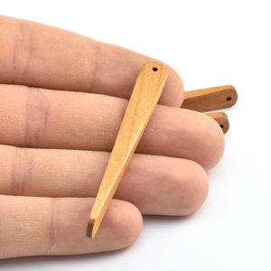 May include: A set of three wooden dowel rods with a pointed tip. The dowels are light brown in color and have a smooth finish.