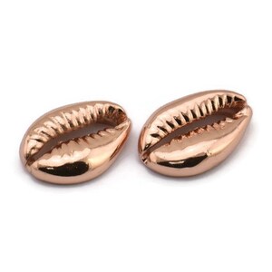 May include: Two rose gold cowrie shell charms. The shells are smooth and shiny with a detailed design.