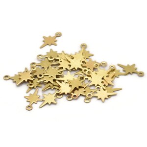 May include: A pile of gold-colored metal star-shaped charms with a loop at the top. The charms are scattered on a white background.