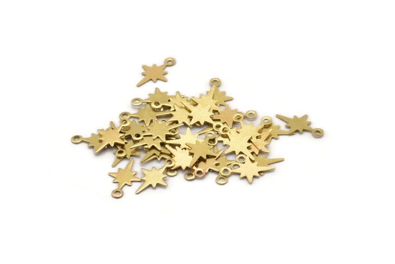 May include: A pile of gold-colored metal star-shaped charms with a loop at the top. The charms are scattered on a white background.